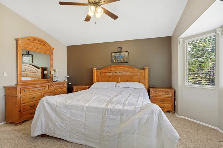 Vaulted ceiling with a ceiling fan, bay window with blinds, and carpeted flooring