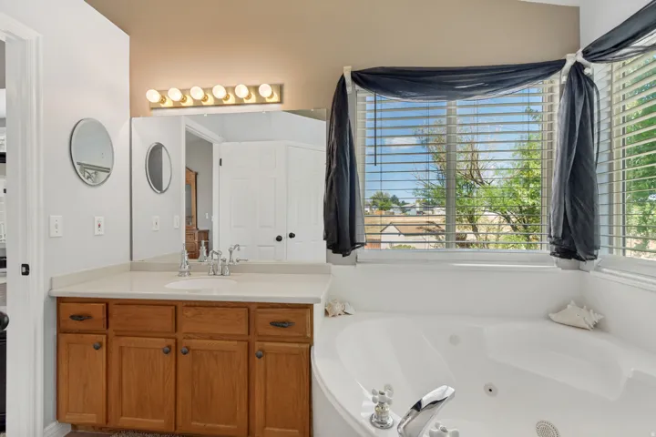 Dual-sink vanity with wood-finish cabinetry, a large mirror, and a corner soaking tub