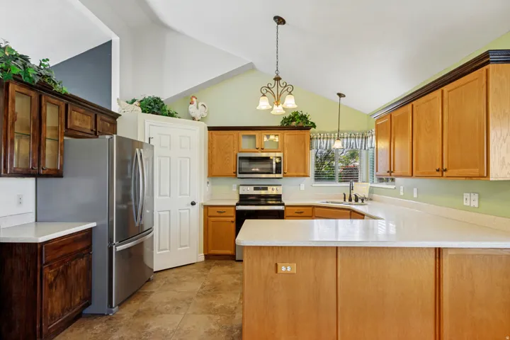 Vaulted ceilings with a decorative chandelier, light wood-finish cabinetry, stainless steel appliances, light-toned countertops, and tile flooring