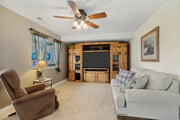 Recessed lighting, wood-finish ceiling fan with integrated light fixture, neutral carpeting, and built-in wood cabinetry with glass-front display