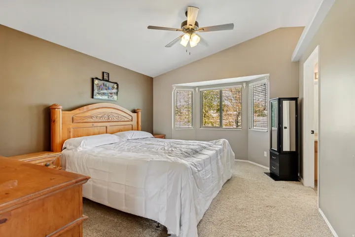 Vaulted ceiling with a ceiling fan, bay window with blinds, and carpeted flooring