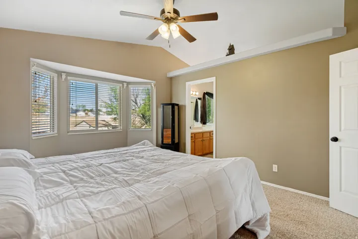 Vaulted ceiling with ceiling fan, bay window with blinds, carpeted flooring, and a six-panel interior door