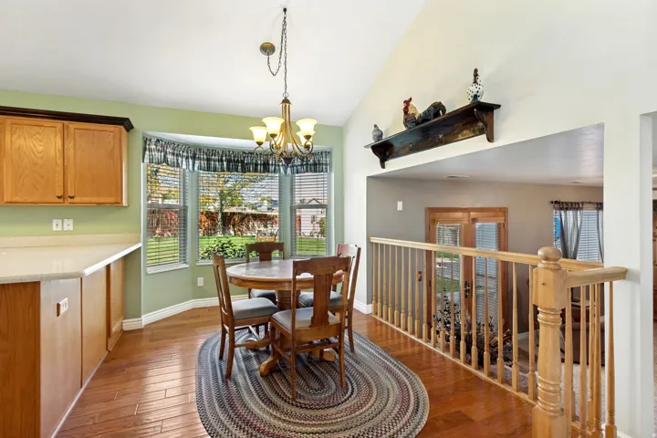 Vaulted ceiling with an overhead light fixture, wood-finish flooring, and a bay window