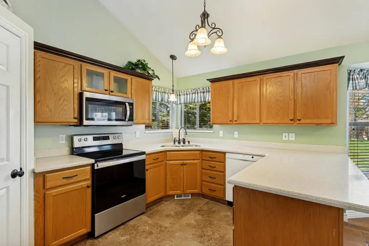 Kitchen featuring wood cabinetry, light-toned countertops, tile flooring, and vaulted ceiling