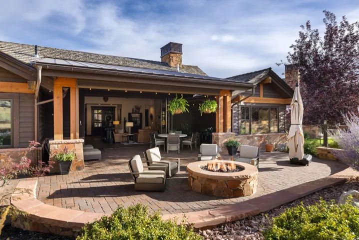 Expansive stone paver patio featuring a built-in stone fire pit, covered outdoor living area, wood siding, and stone accents