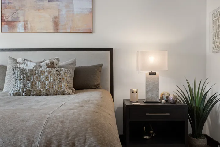 Upholstered headboard with dark wood frame, dark wood-finish nightstand, light-toned walls, and recessed lighting