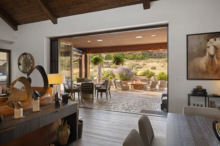Vaulted ceiling with exposed wood beams, wood-finish flooring, and a stone paver patio featuring a built-in fire pit