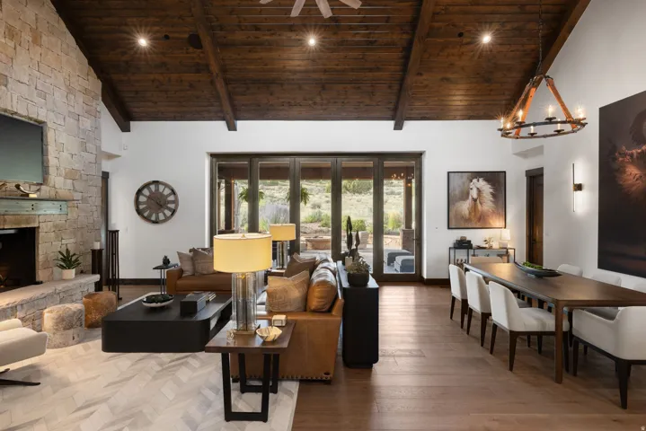 Vaulted wood-beamed ceiling, stone-clad fireplace, wood-finish flooring, and expansive folding glass doors