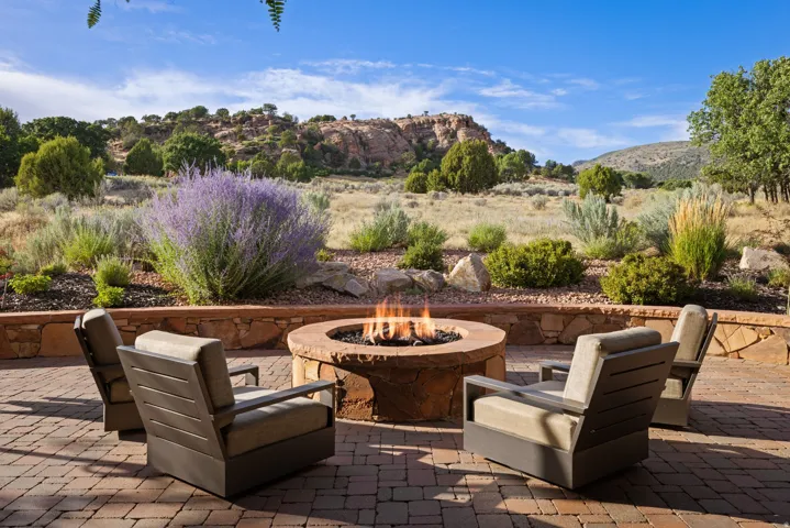 Paver patio featuring a built-in stone fire pit, stone retaining wall, and natural landscaping