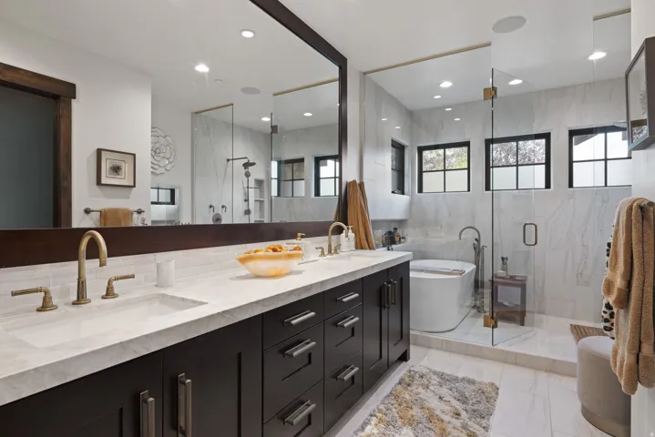 Spa-inspired primary bathroom featuring dual vanities with brushed brass hardware, white quartz countertops, and an expansive framed mirror