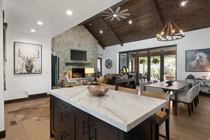 Kitchen island with light-colored countertop, stone fireplace with dark mantel, dark wood vaulted ceiling, large glass folding doors, and wood-finish flooring