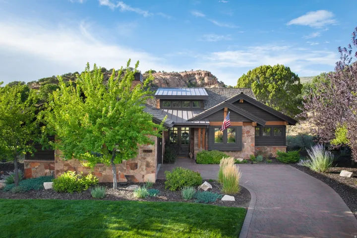 Stone and wood-clad exterior with a dark metal roof, featuring a paver driveway and mature landscaping