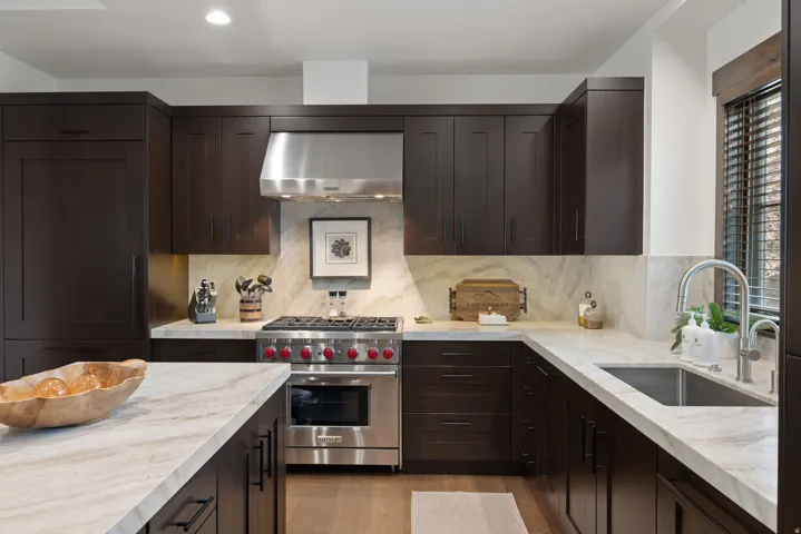 Dark wood cabinetry, light-toned countertops, stainless steel gas range, integrated refrigerator, and a stainless steel sink with a gooseneck faucet