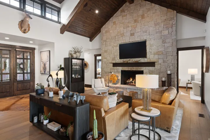 Vaulted wood-beamed ceilings, a floor-to-ceiling stone fireplace, wood-finish flooring, and transom windows