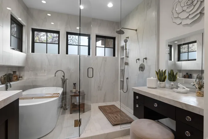 Freestanding soaking tub, walk-in shower with glass enclosure, dual shower heads, integrated shower shelving, and a vanity with built-in storage