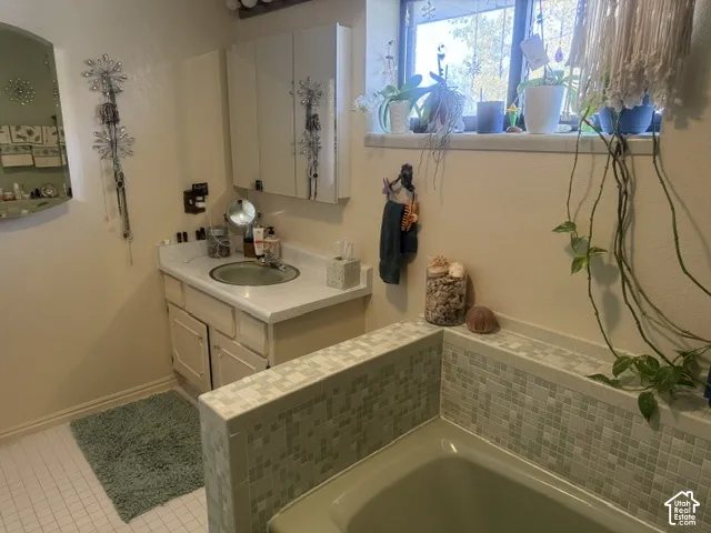 Bathroom featuring a custom-tiled soaking tub with mosaic detailing, a built-in medicine cabinet, an integrated countertop sink, and tile flooring