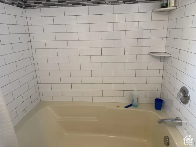 Bathtub surround featuring white subway tile, a multi-tonal glass tile accent border, integrated corner shelving, and polished chrome hardware