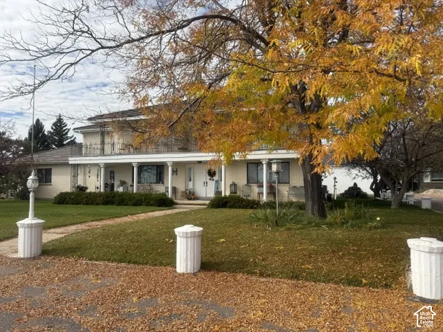 Two-story exterior featuring a covered front porch, decorative white columns, a second-level balcony with metal railing, and brick construction