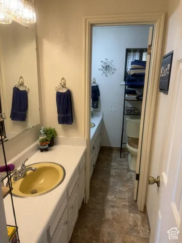 Bathroom featuring white cabinetry, solid-surface countertops with an integrated oval basin, multi-light wall-mounted vanity fixture, and tiled flooring