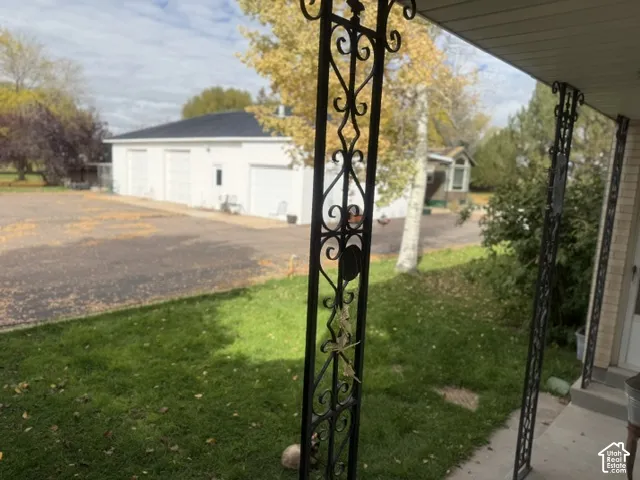 Covered patio with ornamental metal support columns, paved exterior lot, and detached multi-bay structure with metal roofing