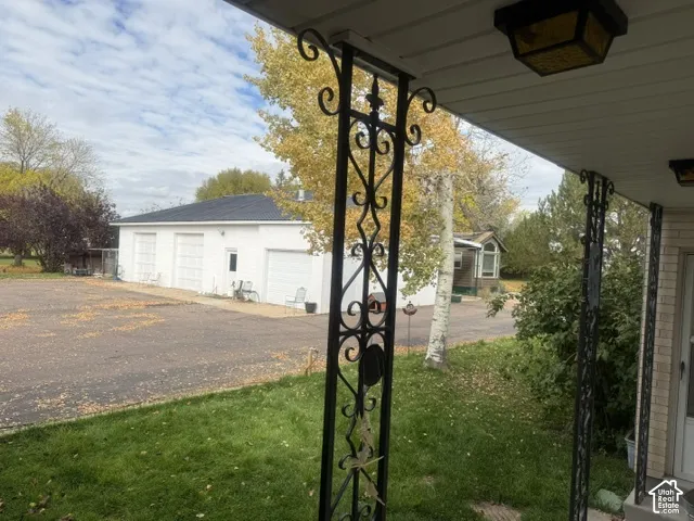 Covered porch featuring ornamental metal support columns and ceiling-mounted exterior lighting, overlooking an expansive asphalt parking area and a detached multi-bay garage