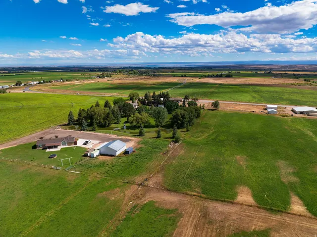 Expansive property featuring a ranch-style residence, large detached outbuilding, and mature trees, surrounded by extensive green fields