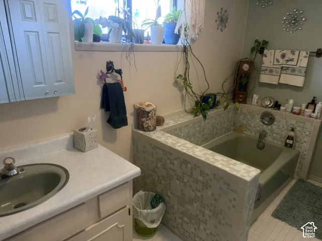 Bathroom featuring a built-in bathtub with glass tile surround, solid-surface vanity countertop, undermount sink, and wall-mounted medicine cabinet