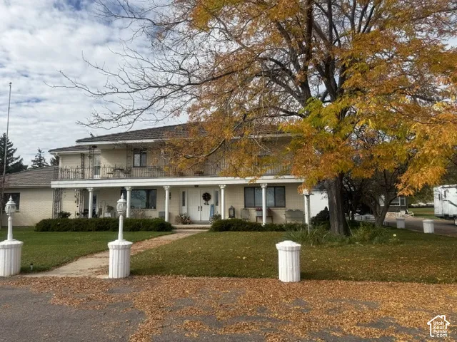Two-story brick exterior featuring a covered front porch, upper-level balcony, decorative columns, and exterior pedestal lighting