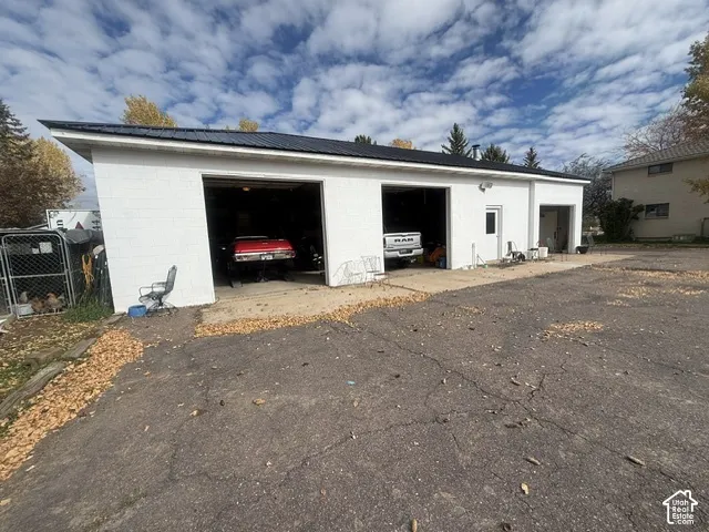 Three-bay detached garage featuring white masonry exterior, dark metal roof, and asphalt-paved approach