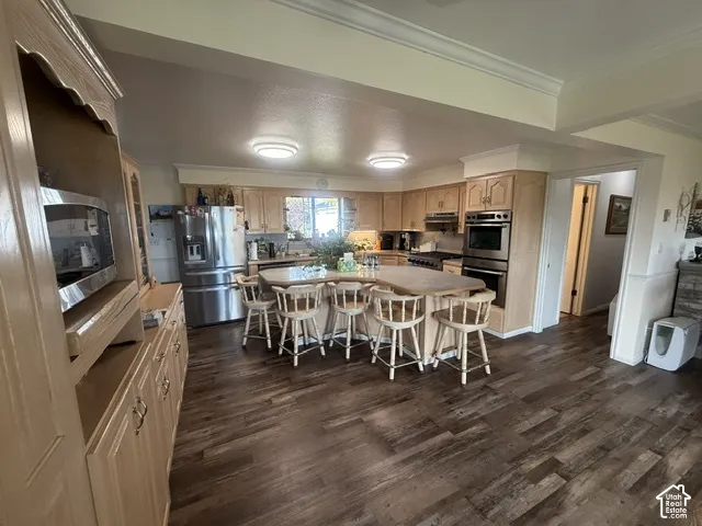 Kitchen featuring custom light wood cabinetry, stone-finish countertops, stainless steel appliances, a central island with bar seating, and wood-finish flooring