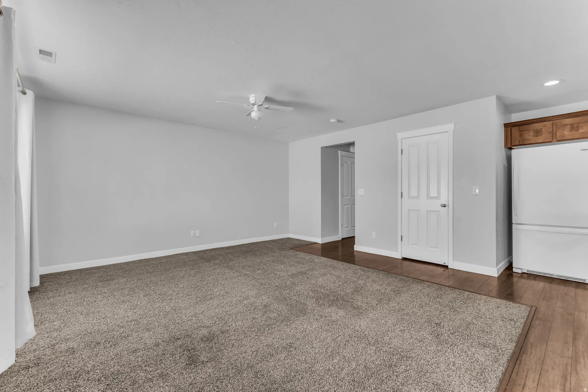 Light gray wall paint, textured carpeting, wood-finish flooring, white paneled doors, and a ceiling fan