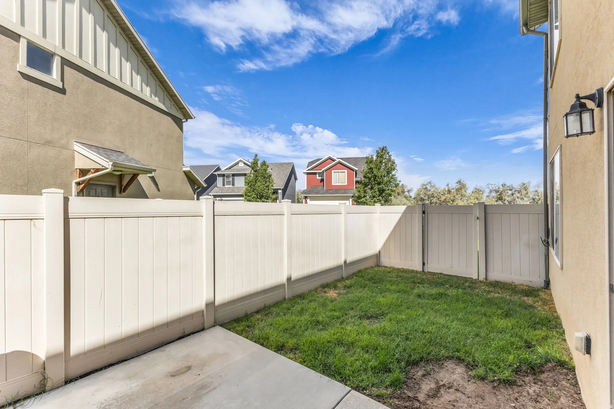 Private fenced yard with concrete patio, grass area, and exterior wall lighting