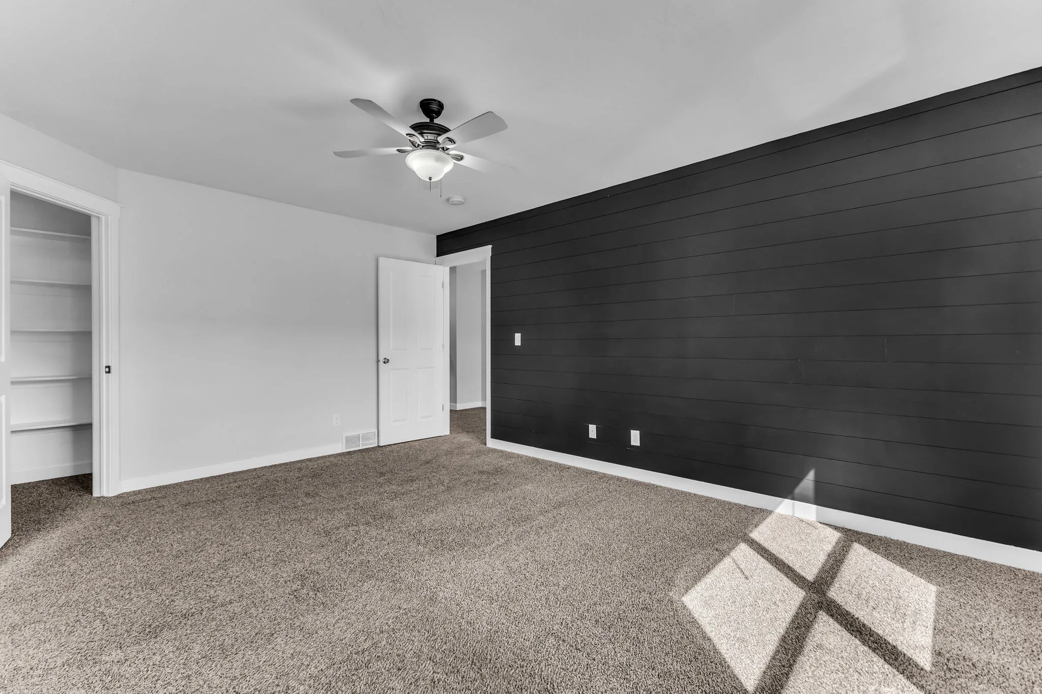 Room featuring plush carpeting, a ceiling fan with integrated lighting, built-in shelving, and a dark accent wall