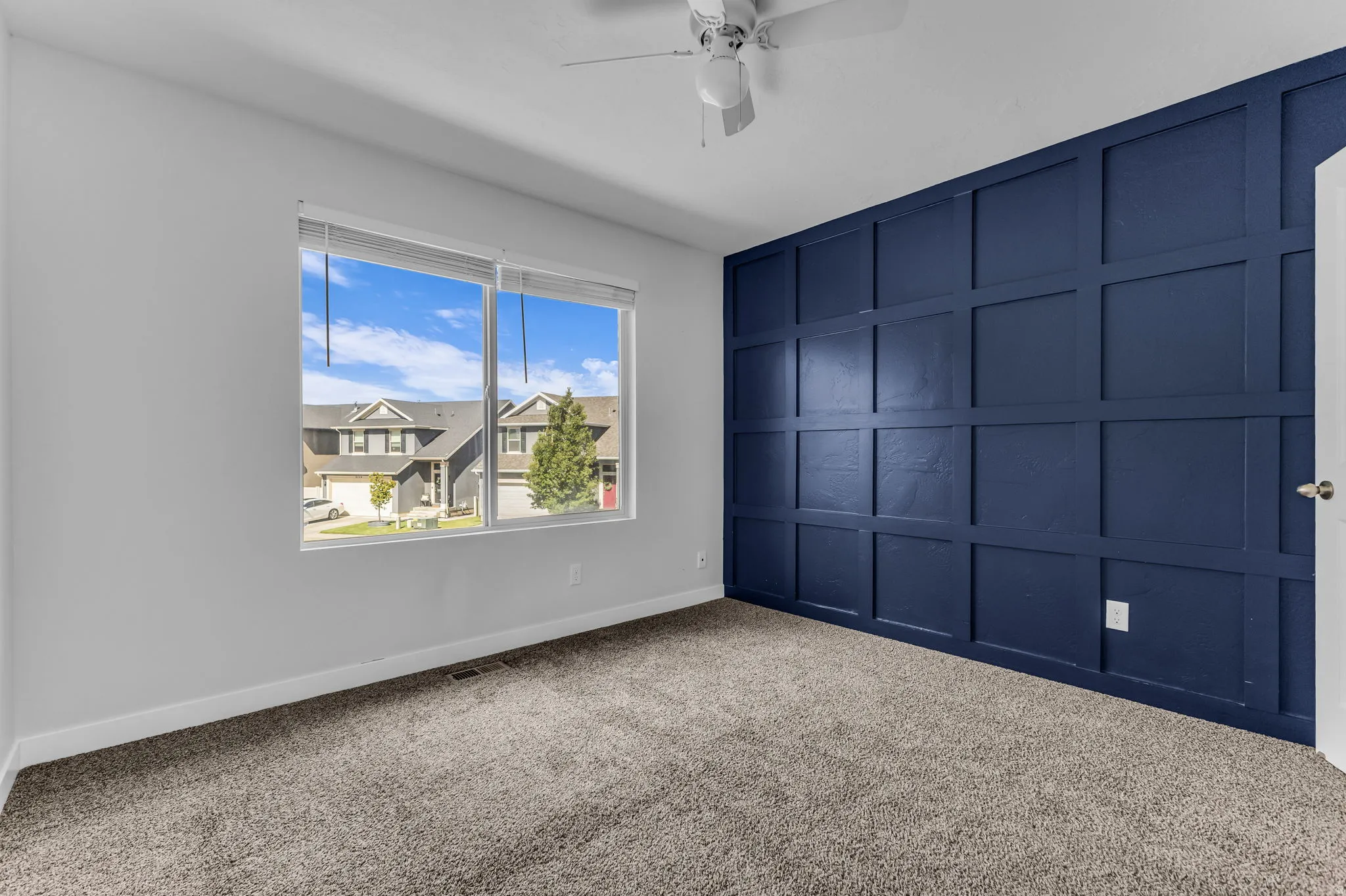 Board and batten accent wall, neutral carpeting, ceiling fan, and large window