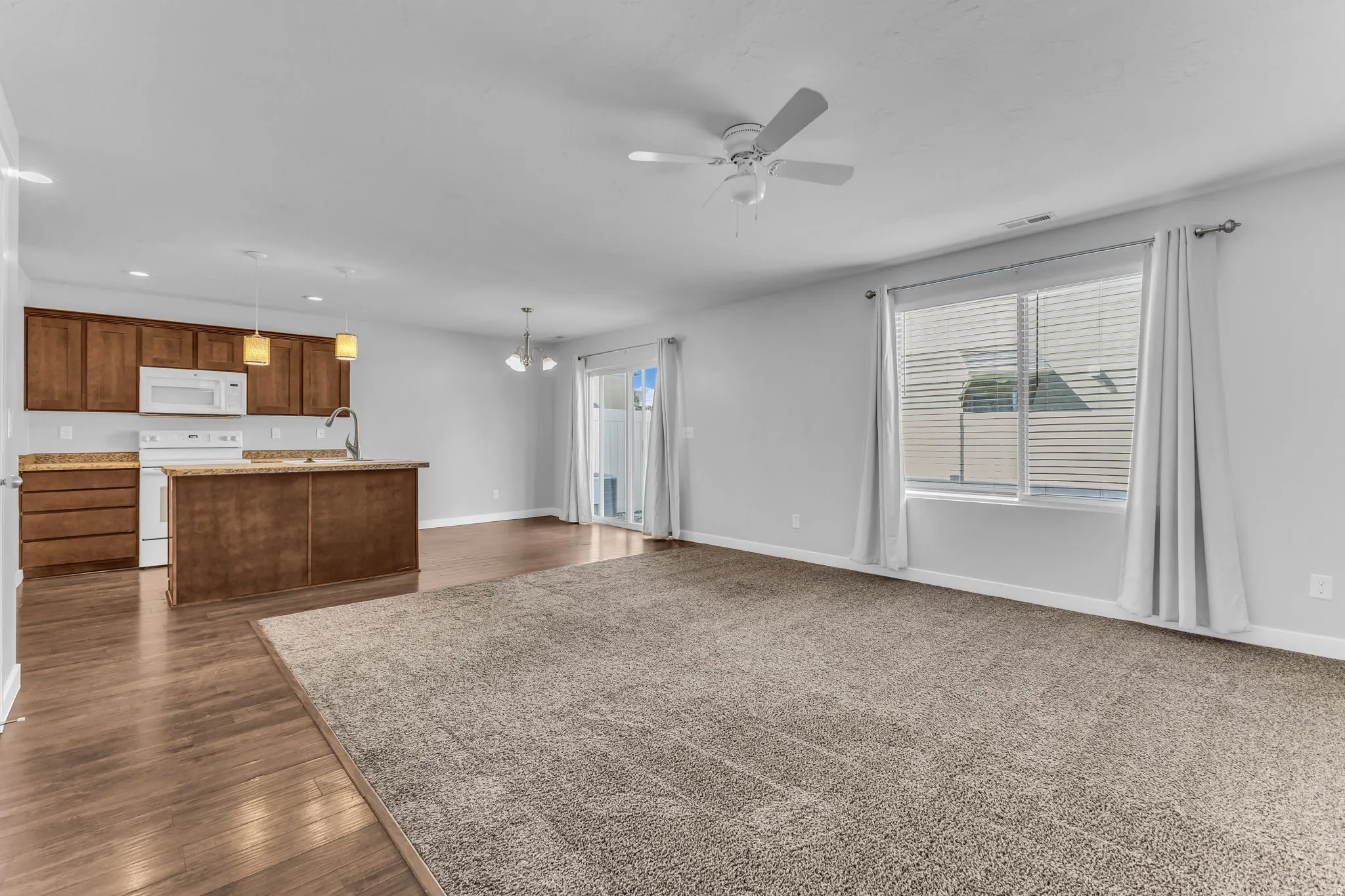 Open-concept living space featuring wood-finish flooring, a kitchen island with stone-finish countertop, white appliances, and a sliding glass door