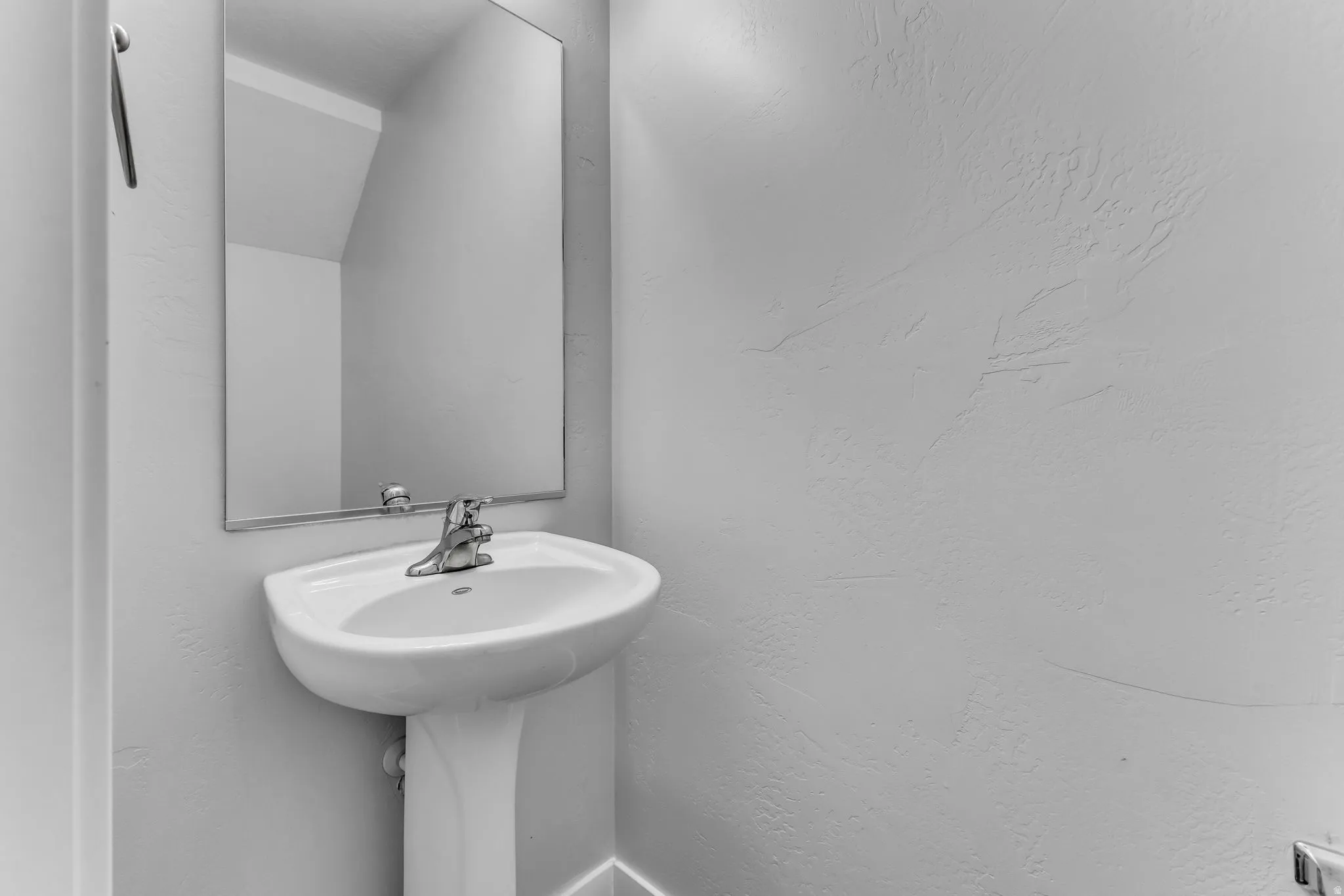 Pedestal sink with chrome faucet, wall-mounted rectangular mirror, and textured wall finish