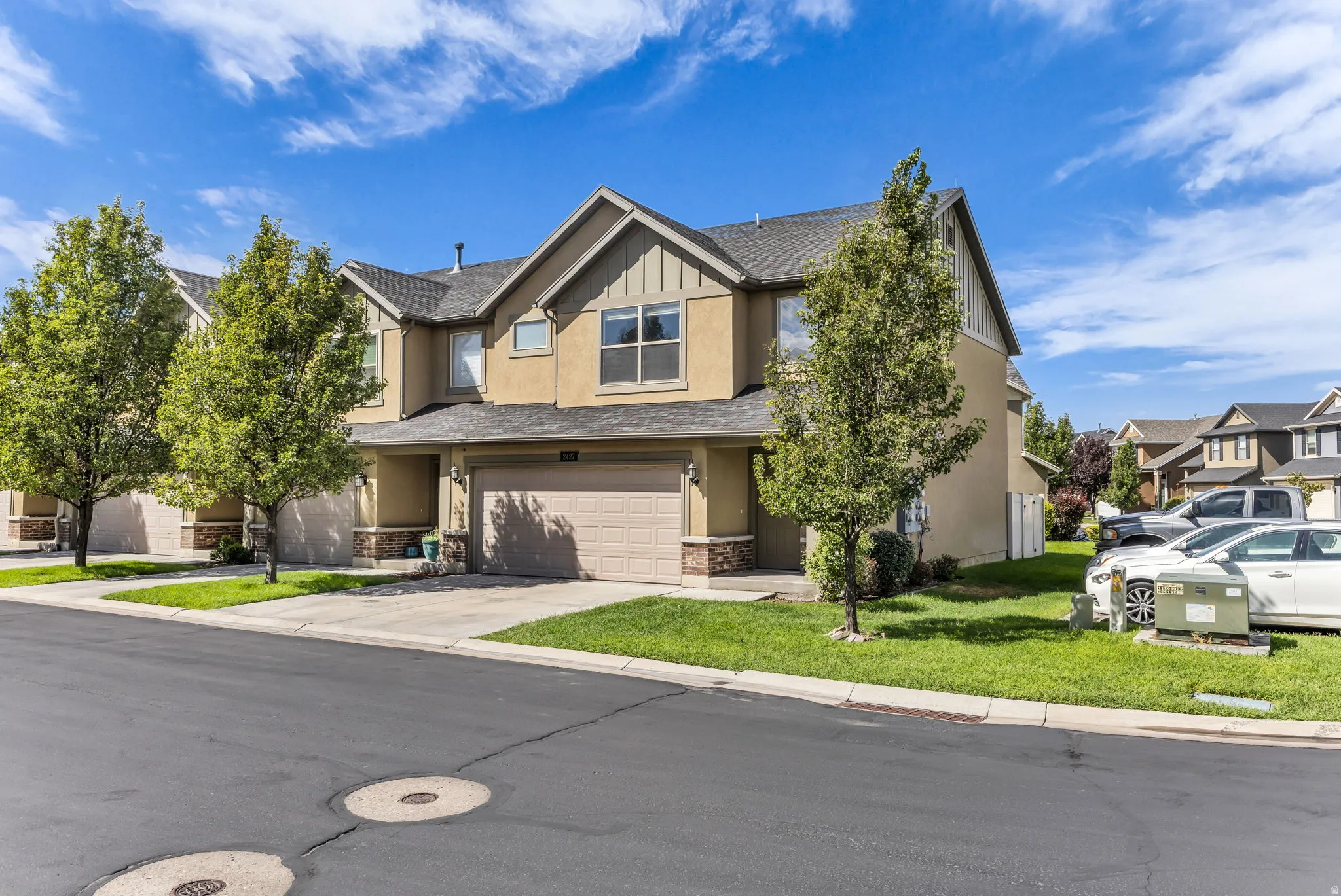 Stucco exterior with stone accents, attached garage, gabled roofline, mature trees, and concrete driveway