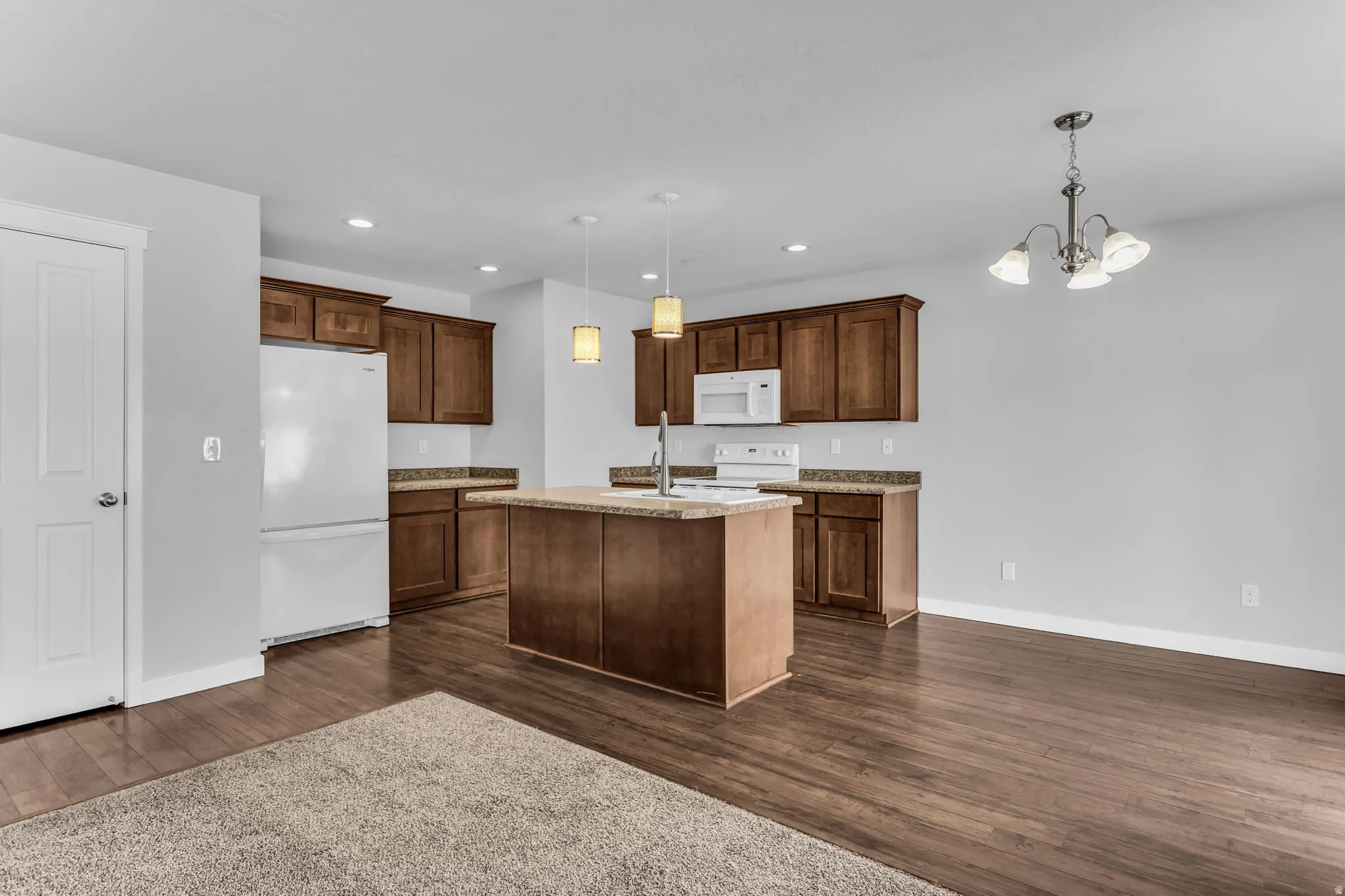 Open-concept kitchen featuring wood-finish cabinetry, a central island, and built-in white appliances
