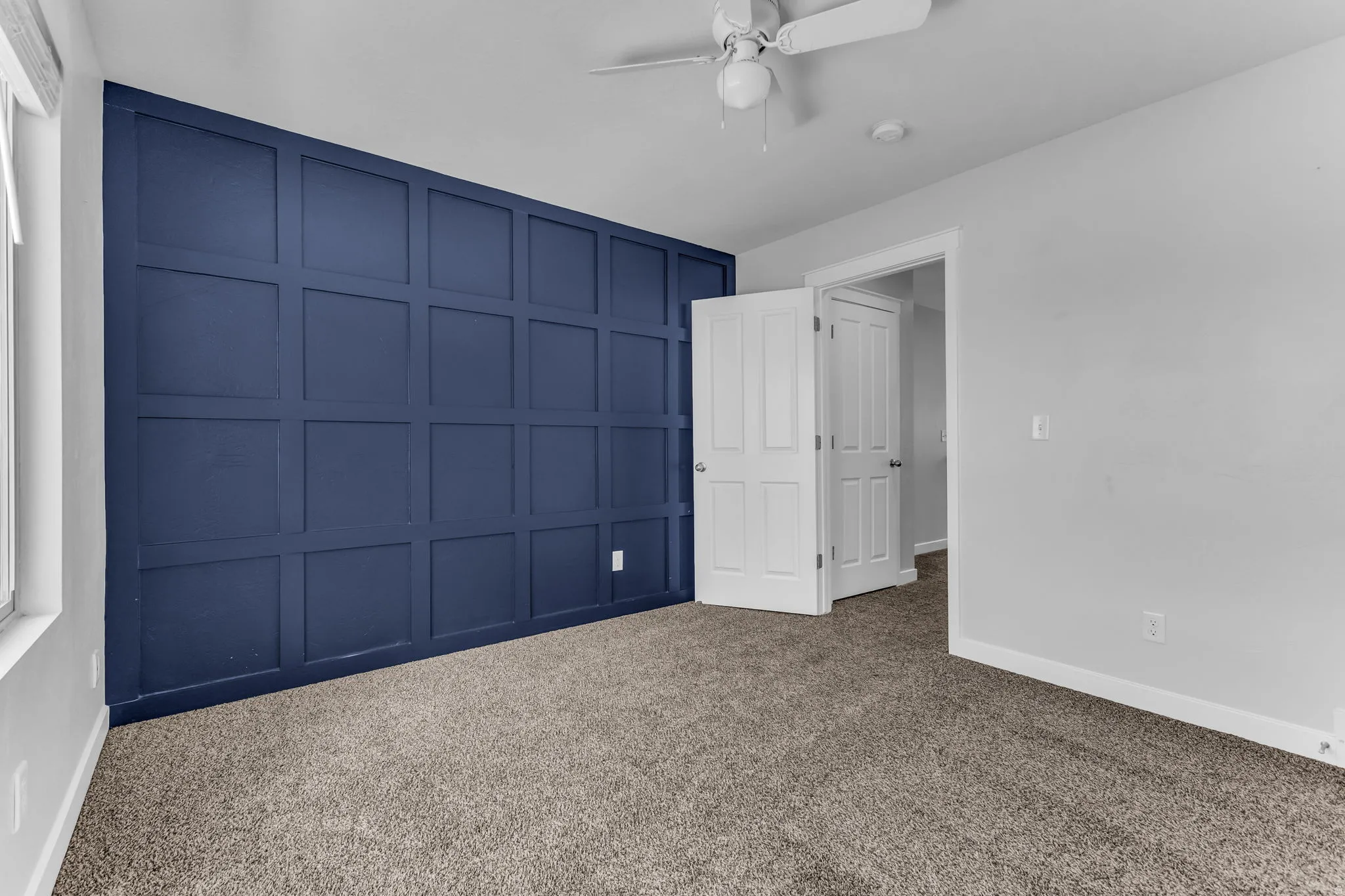 Feature wall with wainscoting, broadloom carpeting, white interior doors, and a ceiling fan