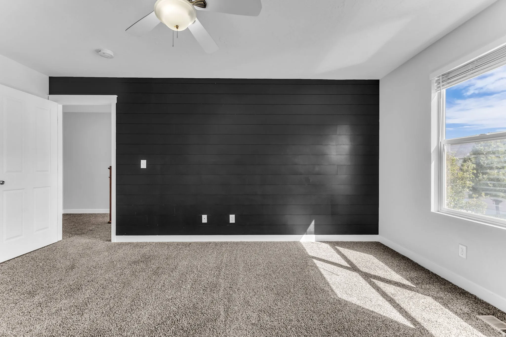 Carpeted flooring, contemporary ceiling fan, accent wall with horizontal paneling, and window with blinds