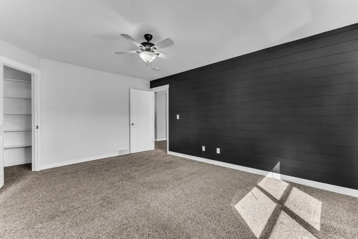 Room featuring plush carpeting, a ceiling fan with integrated lighting, built-in shelving, and a dark accent wall