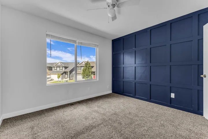 Board and batten accent wall, neutral carpeting, ceiling fan, and large window