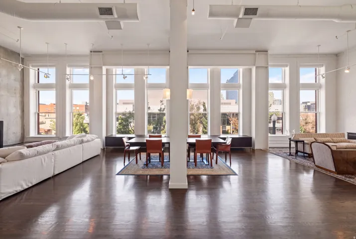 Open-concept living space with dark wood-finish flooring, exposed concrete wall, tall windows, and a column structural element