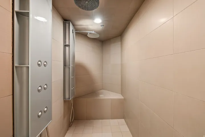 Tiled shower enclosure featuring a built-in corner bench, multiple showerheads, recessed lighting, and integrated vertical body spray panels