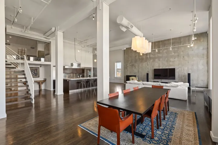 High ceilings, exposed concrete accent wall, wood-finish flooring, open-concept kitchen with island, and a mezzanine level