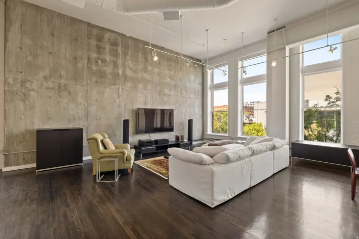Exposed concrete accent wall, high ceilings, dark wood-finish flooring, track lighting, and multiple tall windows