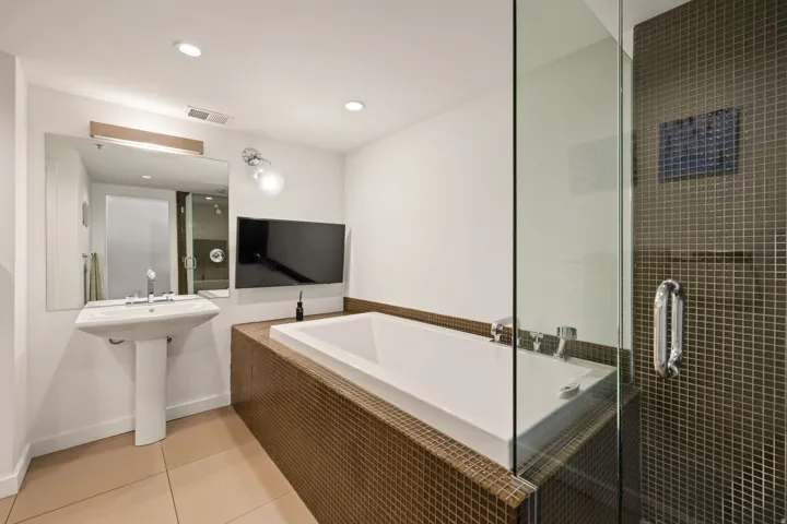 Pedestal sink with chrome fixtures, integrated soaking tub, glass-enclosed shower with mosaic tile, and recessed lighting