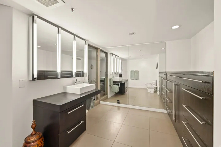 Integrated vanity with vessel sink, wall-mounted medicine cabinets with integrated lighting, extensive built-in storage cabinetry, tiled flooring, and a large wall mirror