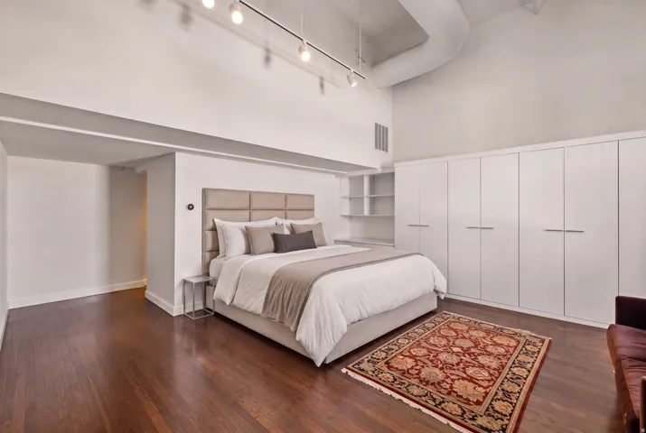 Hardwood flooring with a high ceiling, track lighting, and built-in white cabinetry