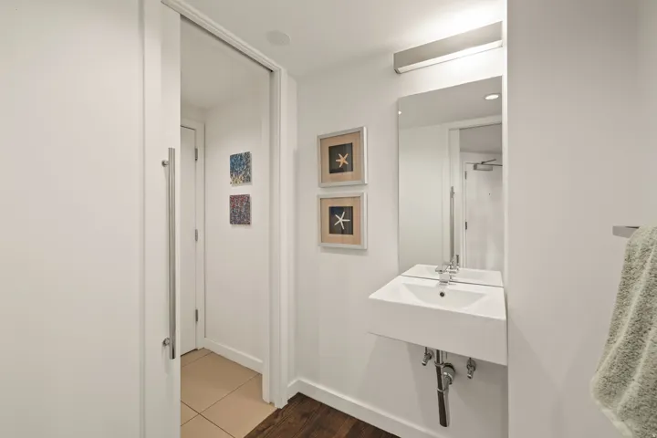 Wall-mounted rectangular sink with chrome faucet, integrated frameless mirror, and a linear vanity light fixture